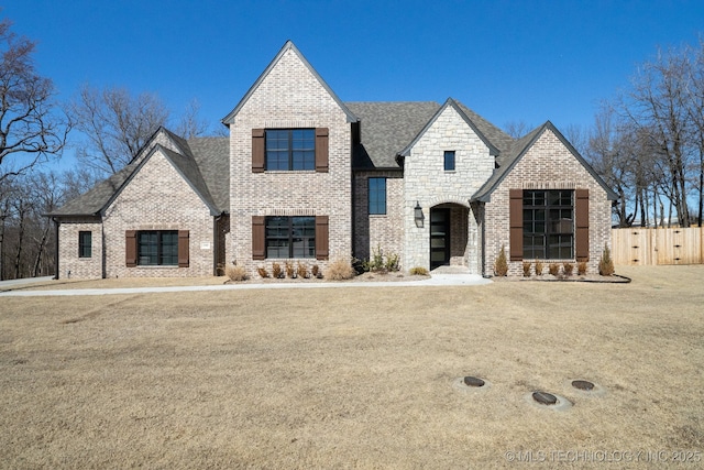 french provincial home with brick siding, roof with shingles, and fence