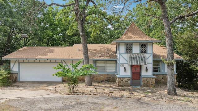 tudor home featuring a garage, concrete driveway, stone siding, roof with shingles, and stucco siding