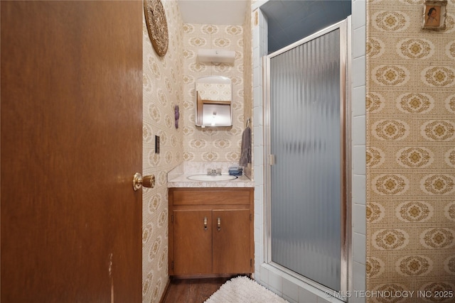 full bath with wallpapered walls, vanity, wood finished floors, and a stall shower