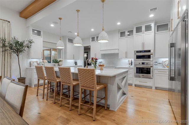 kitchen featuring stainless steel appliances, light countertops, a kitchen island with sink, white cabinets, and light wood-type flooring