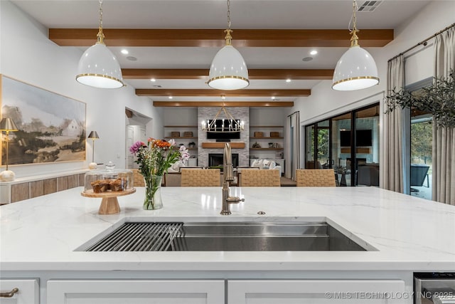 kitchen featuring open floor plan, light stone counters, a sink, and decorative light fixtures