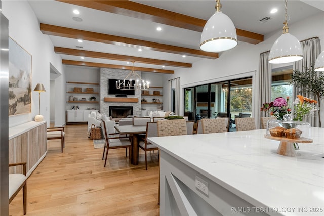 kitchen with a large fireplace, beamed ceiling, visible vents, and light wood-style floors