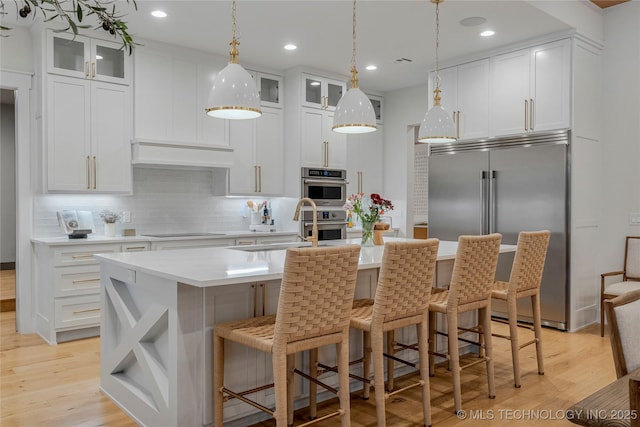 kitchen featuring custom exhaust hood, light countertops, light wood-style flooring, appliances with stainless steel finishes, and a sink