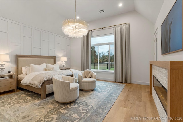 bedroom with visible vents, a glass covered fireplace, lofted ceiling, light wood-style flooring, and a notable chandelier