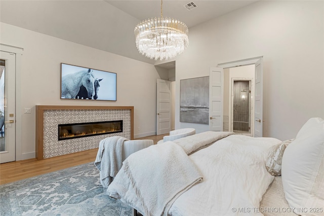 bedroom with visible vents, an inviting chandelier, wood finished floors, a tile fireplace, and baseboards