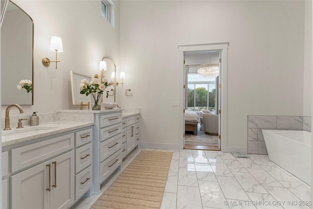 ensuite bathroom with double vanity, baseboards, marble finish floor, a freestanding bath, and a sink