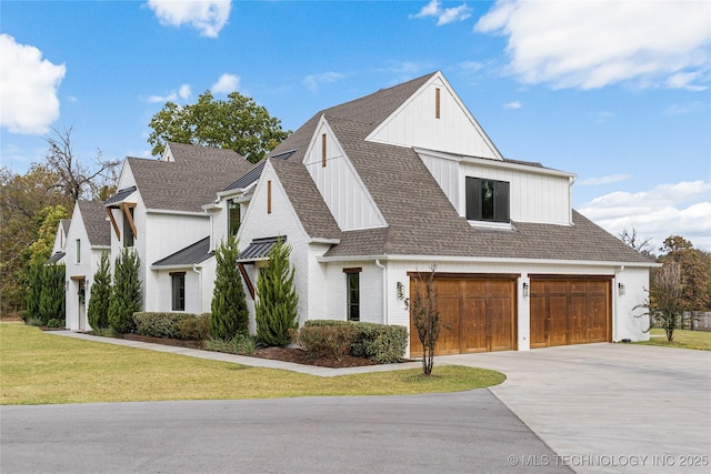 modern inspired farmhouse featuring an attached garage, a shingled roof, brick siding, driveway, and a front lawn