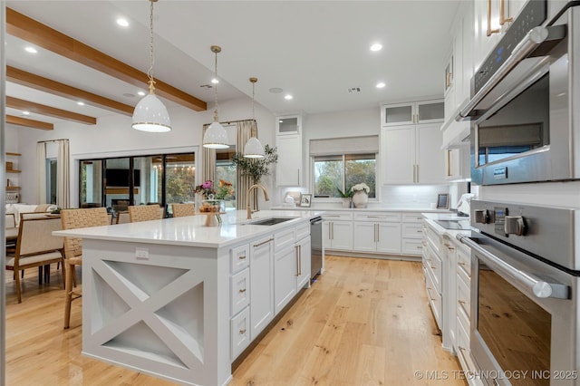 kitchen featuring appliances with stainless steel finishes, a sink, light wood-style flooring, and a center island with sink