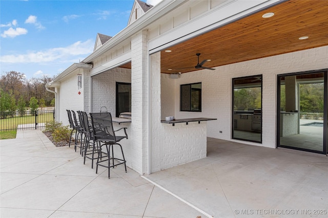 view of patio with exterior bar, fence, and a ceiling fan