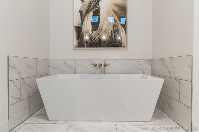 full bathroom featuring marble finish floor, a wainscoted wall, and a soaking tub