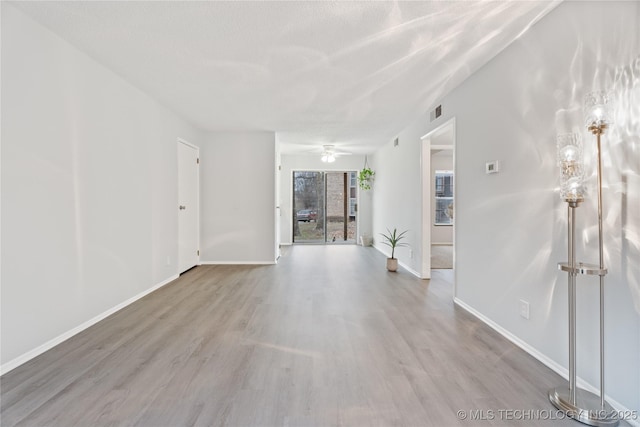 empty room featuring a ceiling fan, wood finished floors, a textured ceiling, baseboards, and visible vents