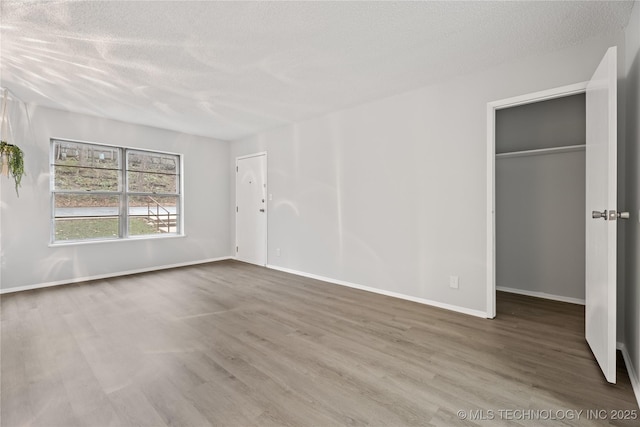 unfurnished bedroom featuring a walk in closet, a textured ceiling, baseboards, and wood finished floors