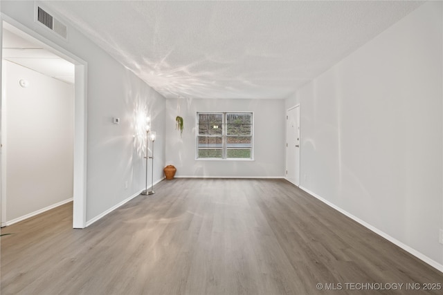 unfurnished room with wood finished floors, a textured ceiling, baseboards, and visible vents