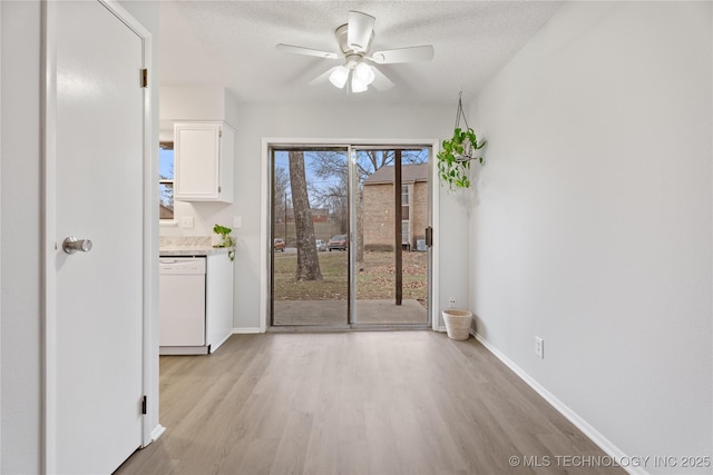 unfurnished dining area with baseboards, a textured ceiling, light wood-style floors, and a ceiling fan