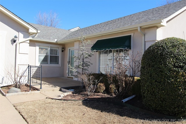 entrance to property with roof with shingles and stucco siding