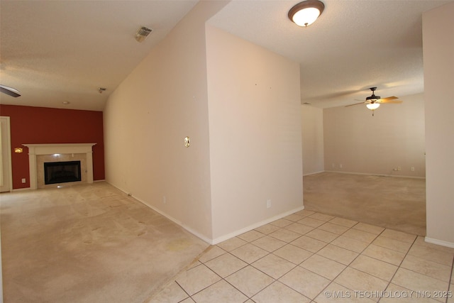 interior space with a textured ceiling, light colored carpet, a fireplace, a ceiling fan, and baseboards