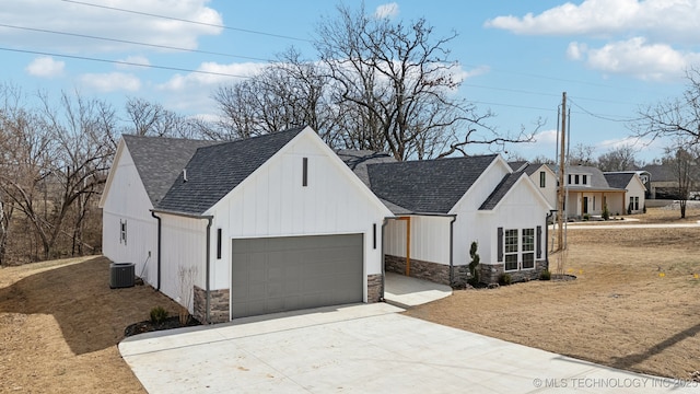 view of front facade featuring stone siding, roof with shingles, concrete driveway, and central air condition unit