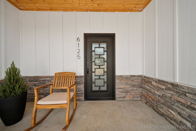 entrance to property with stone siding, board and batten siding, and a patio