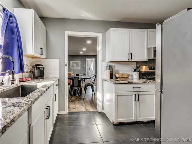 kitchen featuring light stone countertops, tasteful backsplash, white cabinets, and freestanding refrigerator