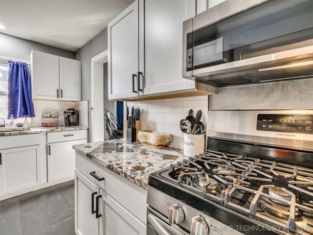 kitchen featuring white cabinets, light stone counters, appliances with stainless steel finishes, tile patterned floors, and backsplash