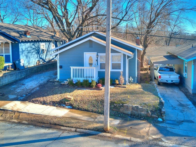 view of front of house with covered porch, a carport, brick siding, and a chimney