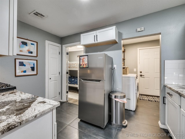 kitchen featuring visible vents, freestanding refrigerator, white cabinets, light stone countertops, and washer and dryer