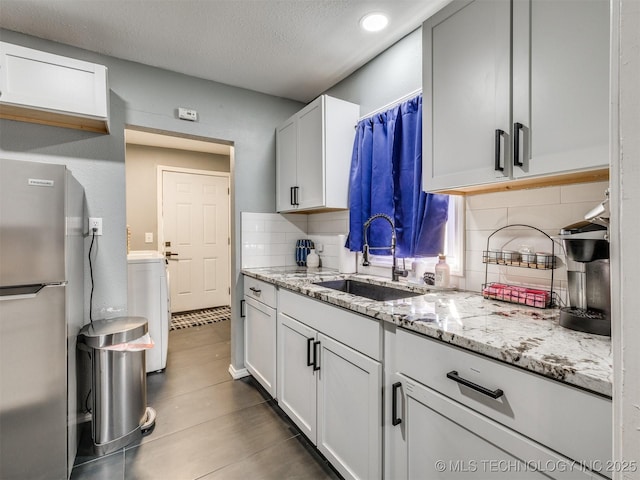 kitchen featuring light stone counters, tasteful backsplash, washer / clothes dryer, freestanding refrigerator, and a sink