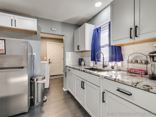 kitchen with light stone counters, a sink, freestanding refrigerator, and white cabinets