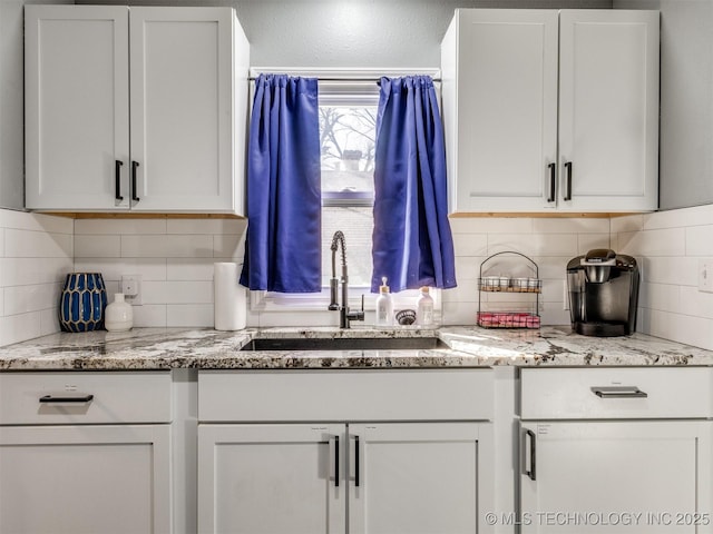 kitchen featuring light stone countertops, white cabinetry, decorative backsplash, and a sink