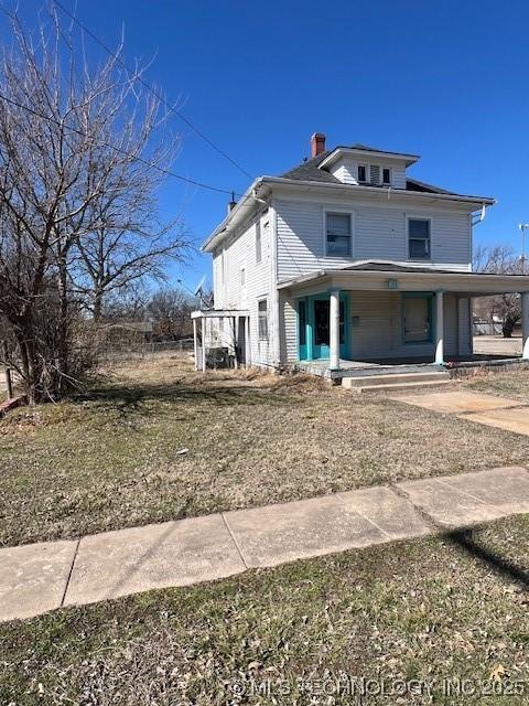 back of house featuring a porch, an attached carport, driveway, and a chimney