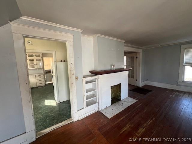 unfurnished living room with wood-type flooring, baseboards, crown molding, and a fireplace with flush hearth