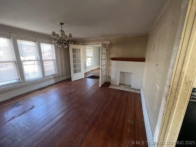 unfurnished living room featuring baseboards, dark wood-style flooring, crown molding, a fireplace, and a notable chandelier