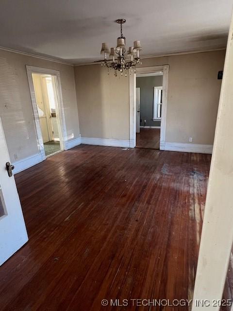 unfurnished dining area featuring baseboards, crown molding, hardwood / wood-style floors, and an inviting chandelier