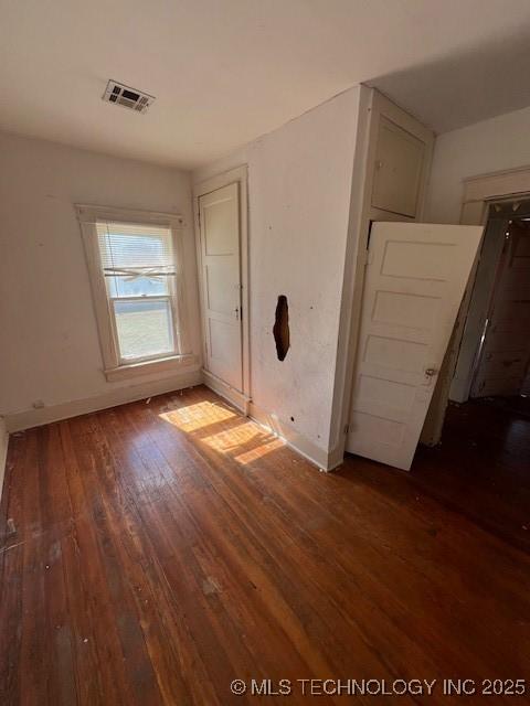 empty room with dark wood-style floors, baseboards, and visible vents