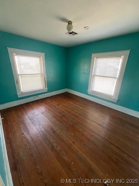 empty room featuring dark wood-type flooring, visible vents, plenty of natural light, and baseboards