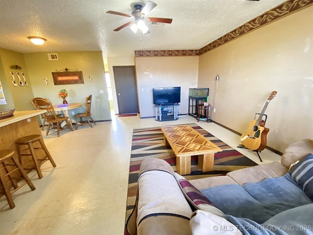 living area featuring baseboards, visible vents, a ceiling fan, tile patterned floors, and a textured ceiling