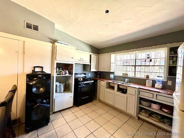 kitchen featuring visible vents, gas stove, vaulted ceiling, a sink, and light tile patterned flooring