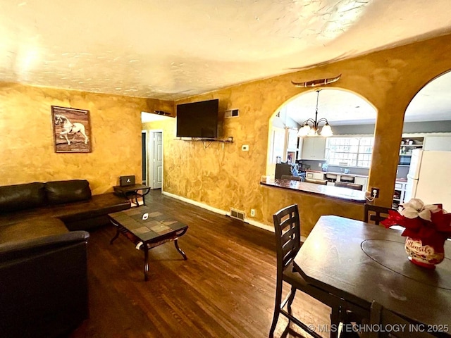 living room featuring an inviting chandelier, visible vents, arched walkways, and wood finished floors