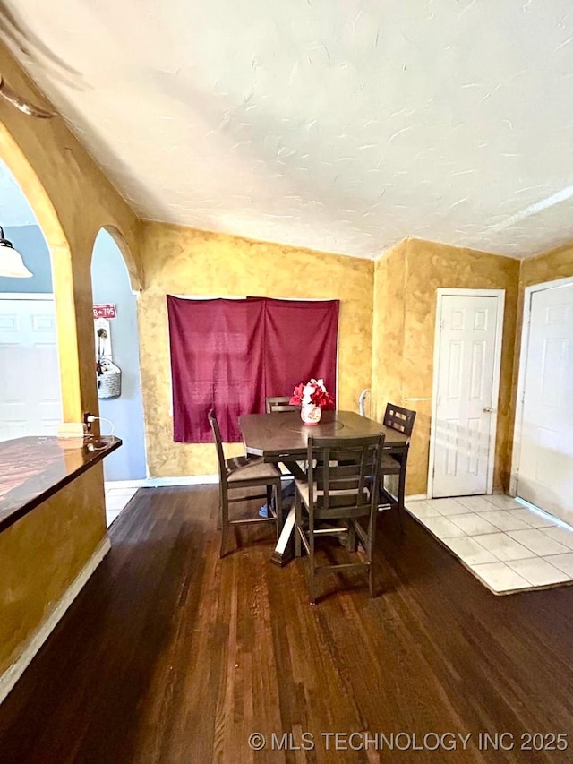 dining area with baseboards, arched walkways, and wood finished floors