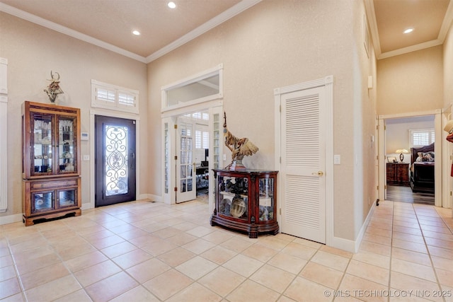 entrance foyer featuring baseboards, a high ceiling, ornamental molding, and light tile patterned flooring