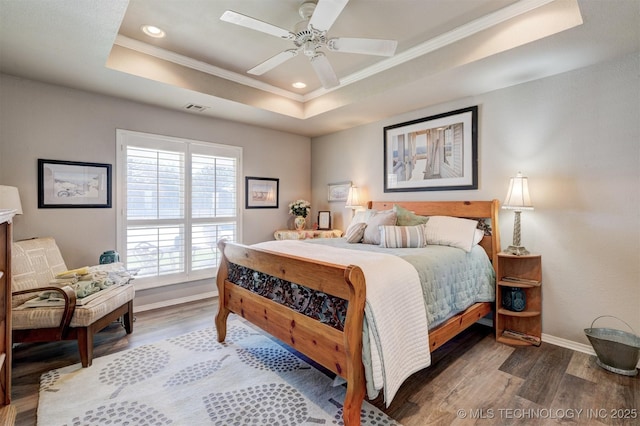 bedroom with a raised ceiling, visible vents, ornamental molding, wood finished floors, and baseboards