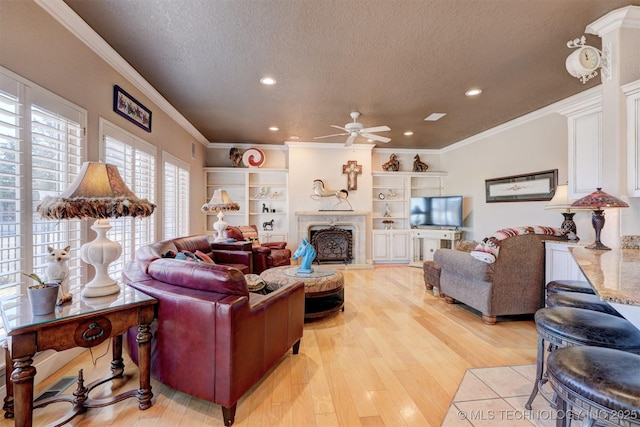 living room with a textured ceiling, light wood-type flooring, a fireplace, and crown molding