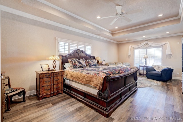 bedroom with baseboards, ornamental molding, a raised ceiling, and wood finished floors