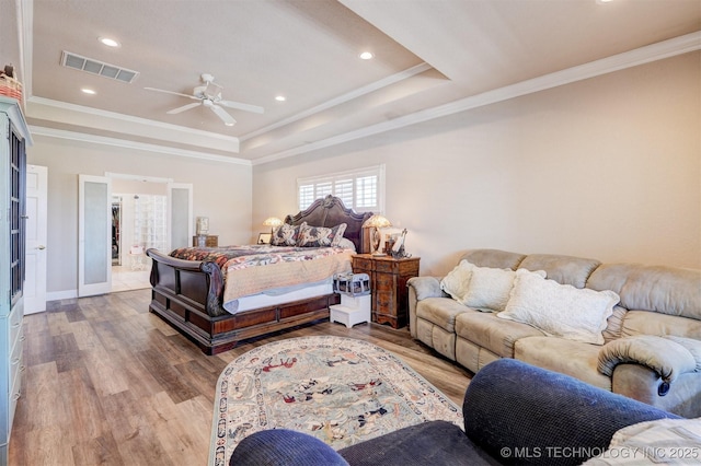 bedroom with ornamental molding, a tray ceiling, visible vents, and wood finished floors