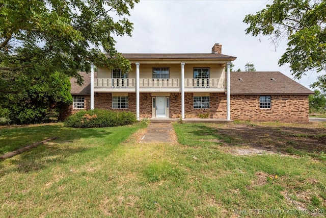 view of front of house featuring a balcony, brick siding, a chimney, and a front yard