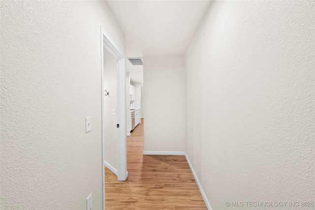 hallway with light wood-type flooring, baseboards, visible vents, and a textured wall