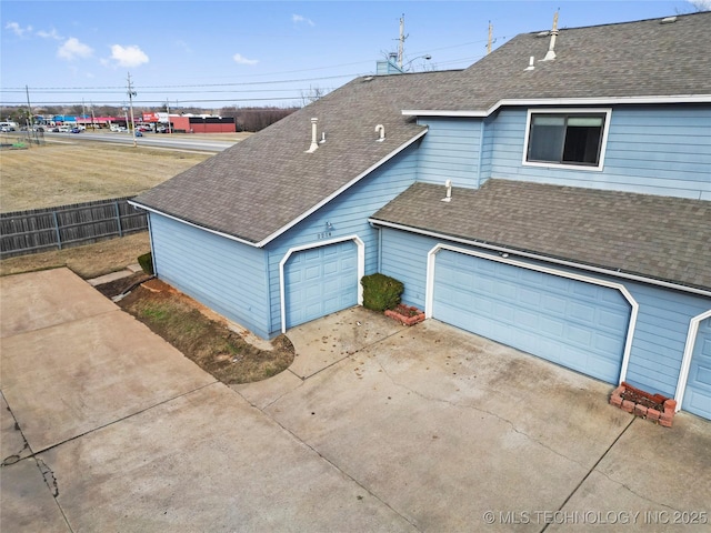 exterior space with a garage, roof with shingles, and fence