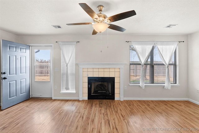 unfurnished living room featuring a tiled fireplace, wood finished floors, visible vents, and baseboards