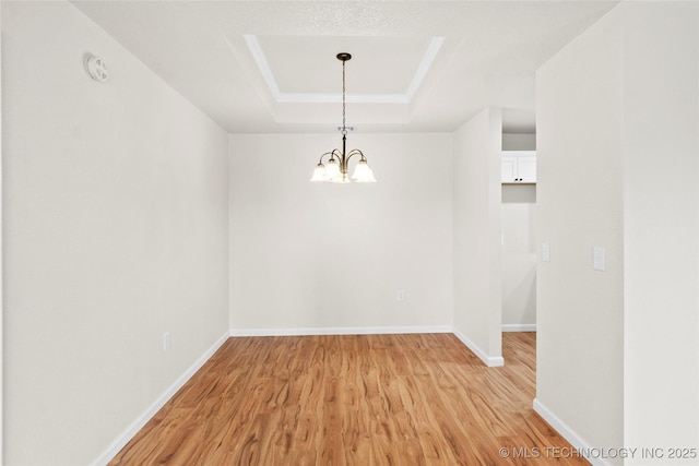 unfurnished dining area with a chandelier, a tray ceiling, light wood-type flooring, and baseboards