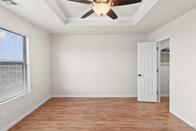 spare room with a tray ceiling, light wood-style flooring, visible vents, and baseboards